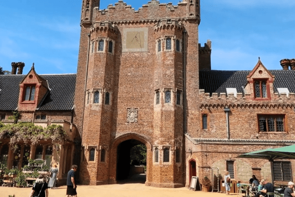 Entrance tower of Oxburgh Hall with red brick walls, arched gateway, and visitors gathered in the courtyard.