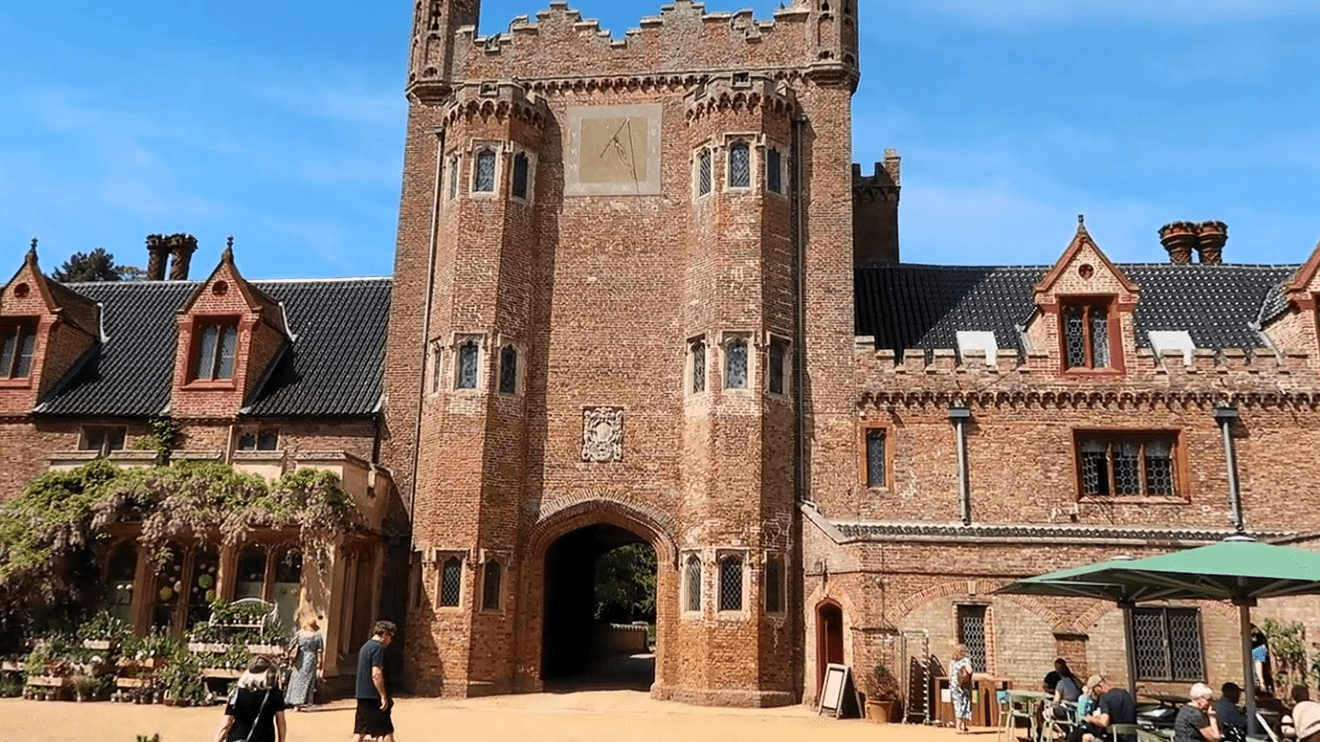 Entrance tower of Oxburgh Hall with red brick walls, arched gateway, and visitors gathered in the courtyard.