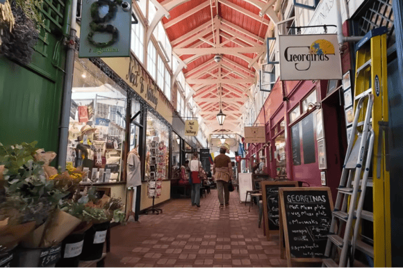 Interior of Oxford Covered Market with independent shops, cafés, colourful storefronts and visitors beneath its historic covered walkway.