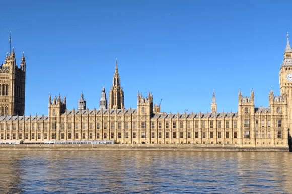 Palace of Westminster and Big Ben viewed across the River Thames under a clear blue sky in London.