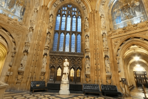 Interior of Palace of Westminster featuring Gothic arches, stained glass windows, and central statue in Westminster Hall.