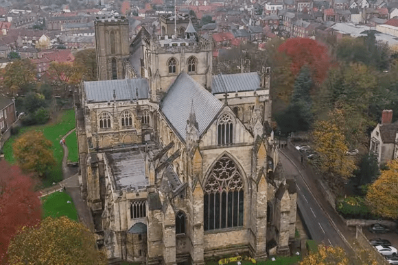Aerial view of Ripon Cathedral in North Yorkshire, England, showing Gothic architecture, large stained-glass windows, and surrounding historic town.