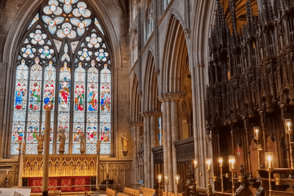 Interior of Ripon Cathedral in North Yorkshire, England, featuring stained glass windows, Gothic arches, choir stalls, and ornate altar.