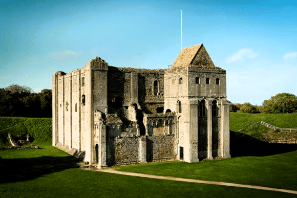 Castle Rising Castle in Norfolk, England, featuring a well-preserved Norman stone keep surrounded by grassy earthworks under clear blue skies.