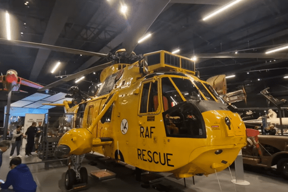 Bright yellow RAF Rescue helicopter displayed inside the Royal Air Force Museum London, surrounded by historic aircraft exhibits and visitors exploring British aviation history.