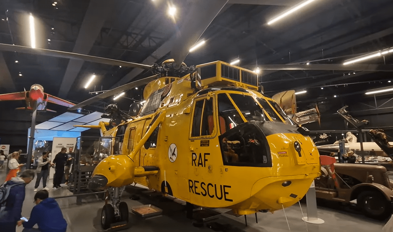 Bright yellow RAF Rescue helicopter displayed inside the Royal Air Force Museum London, surrounded by historic aircraft exhibits and visitors exploring British aviation history.