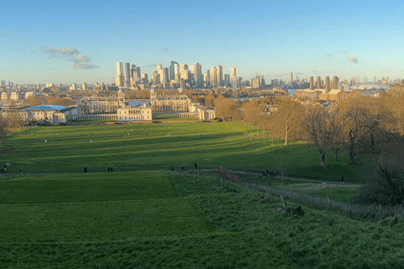 View of Royal Observatory Greenwich across Greenwich Park with London skyline and Canary Wharf in the background.