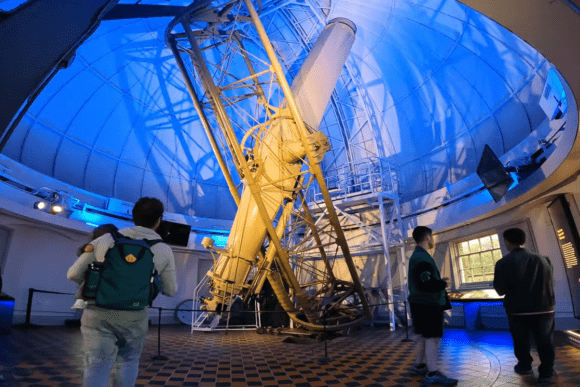 Interior of Royal Observatory Greenwich showing historic telescope inside domed observatory with visitors viewing exhibits in London.
