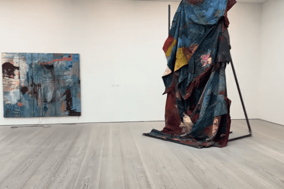 Contemporary mixed-media installation at Saatchi Gallery in London featuring a large draped textile sculpture with layered colours alongside an abstract painting in a minimalist exhibition space.