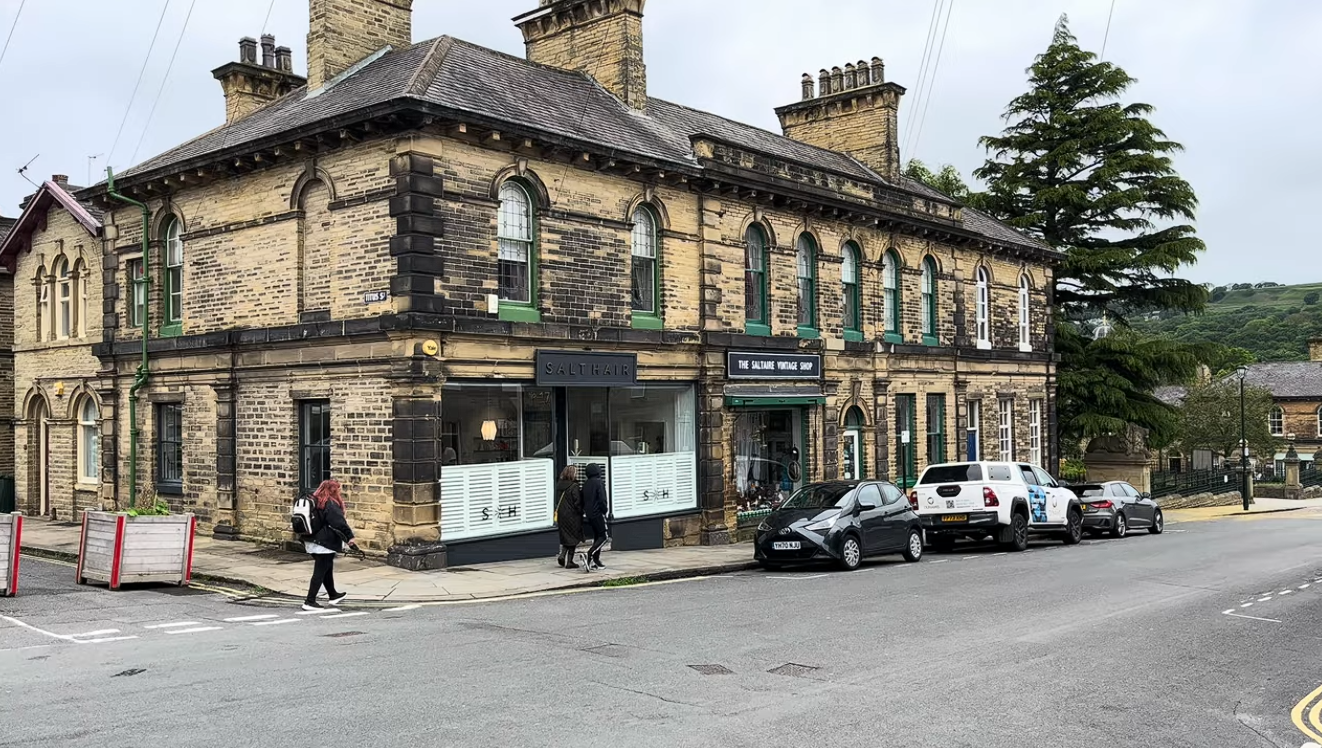 Historic stone building with shops and pedestrians in Saltaire village, West Yorkshire, a UNESCO World Heritage Site.