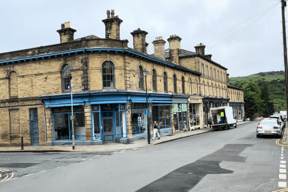 Victorian stone buildings with blue shopfronts along a quiet street in Saltaire, West Yorkshire UNESCO World Heritage village.