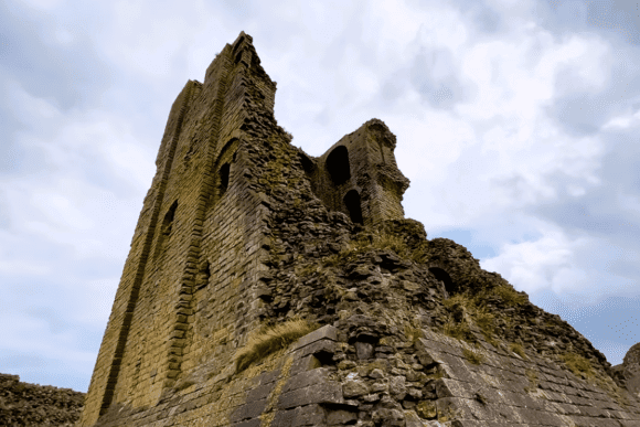 Stone ruins of Scarborough Castle tower rising against a cloudy sky in North Yorkshire, England.