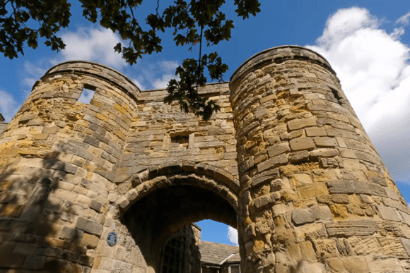 Historic stone gatehouse entrance of Scarborough Castle with round towers under a blue sky in North Yorkshire.