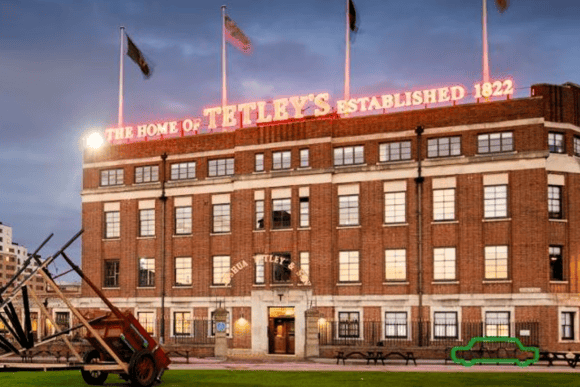 The Tetley historic brewery building in Leeds South Bank at dusk, featuring its illuminated rooftop sign and public artwork outside.