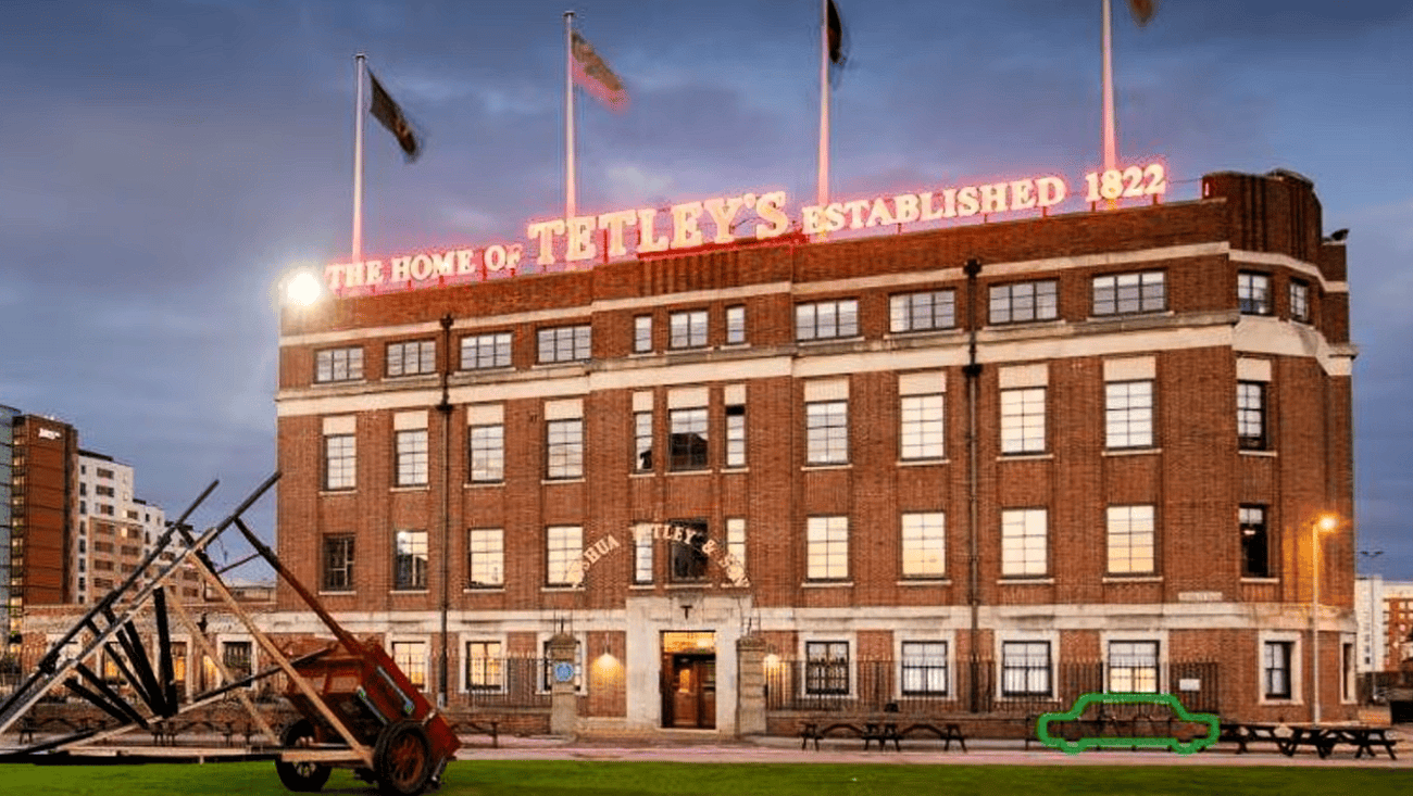 The Tetley historic brewery building in Leeds South Bank at dusk, featuring its illuminated rooftop sign and public artwork outside.