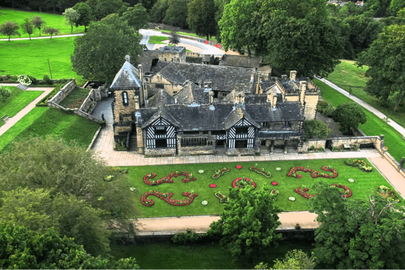Aerial view of Shibden Hall with Tudor architecture, landscaped gardens, and decorative flower beds in Halifax.