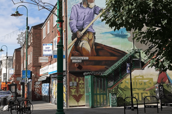 Colourful street art mural beside a green staircase on Hopetown Street in Shoreditch, East London, surrounded by shops and urban architecture.