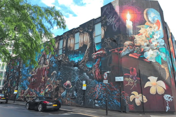Large colourful street art mural covering a building in Shoreditch, London, featuring flowers, mushrooms and surreal artwork on King John Court.