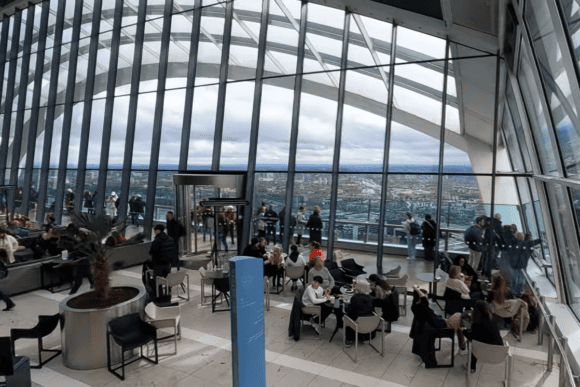 Interior of Sky Garden, London, with floor-to-ceiling glass windows, visitors dining and sightseeing, and panoramic views across the London skyline.