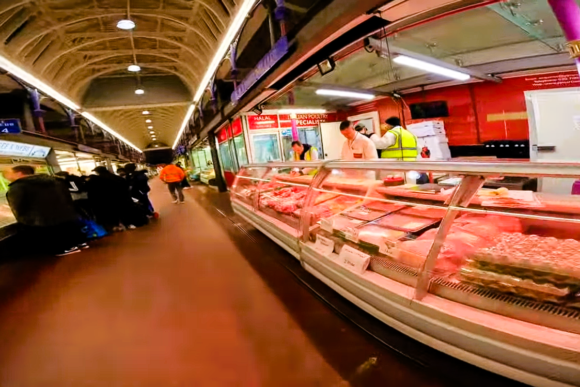 Busy interior of Smithfield Market London with meat stalls, glass display counters, and vendors serving customers.