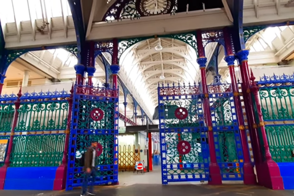 Interior of Smithfield Market London with ornate colourful iron gates, Victorian architecture, and high vaulted ceiling.