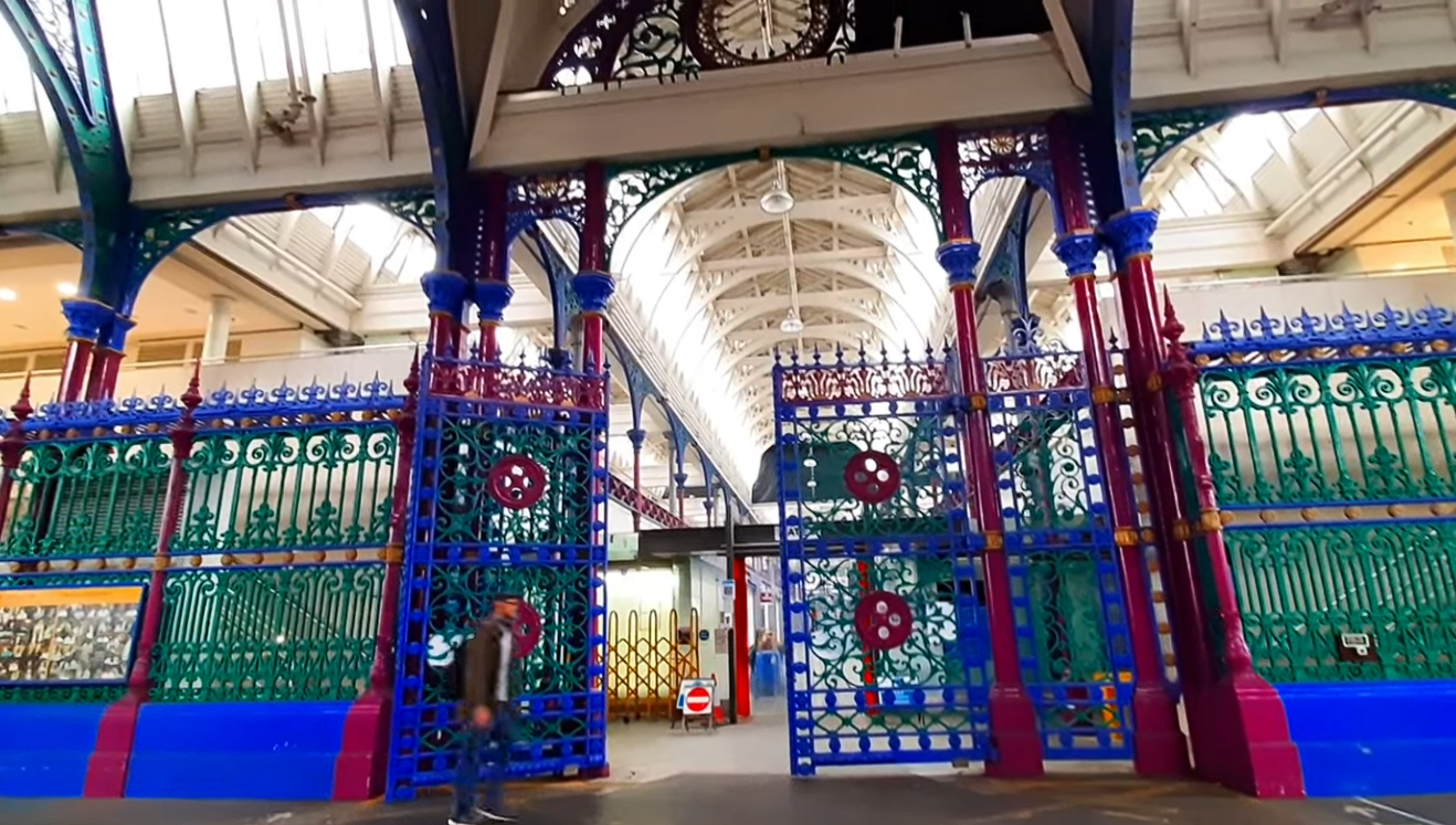 Interior of Smithfield Market London with ornate colourful iron gates, Victorian architecture, and high vaulted ceiling.