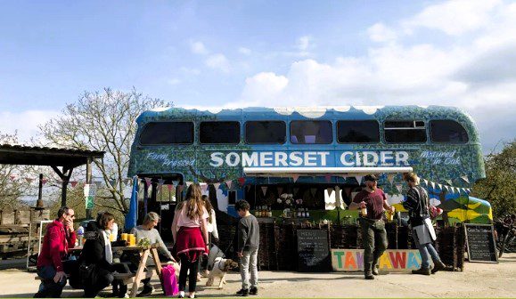 Vintage Somerset Cider double-decker bus serving drinks and refreshments at the Somerset Cider Brandy Company, with visitors enjoying outdoor seating in the Somerset countryside.