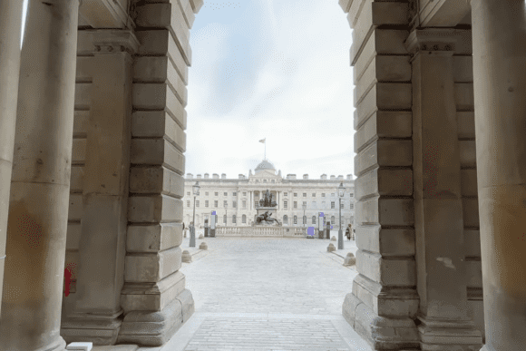 View through stone archway at Somerset House London courtyard with statue and neoclassical building in the background.