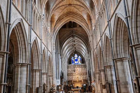 Southwark Cathedral nave London with soaring Gothic arches, stone columns, stained glass window, and ornate high altar.
