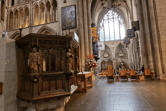 Interior of Southwark Cathedral London with carved wooden pulpit, Gothic arches, stained glass window, and seating area.