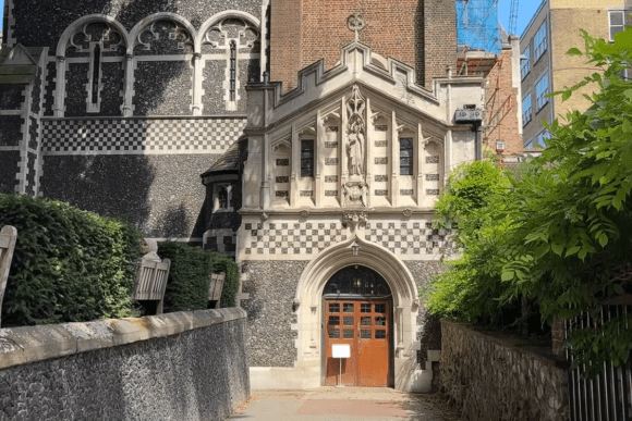 St Bartholomew-the-Great church entrance London with Gothic arch doorway, decorative stone facade, and flint walls.