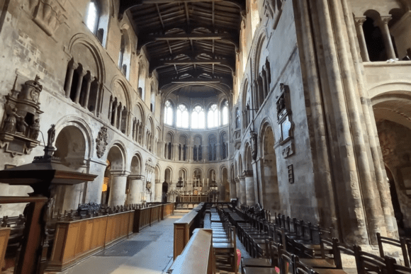 Interior of St Bartholomew-the-Great London with Romanesque arches, wooden pews, and historic nave leading to altar.