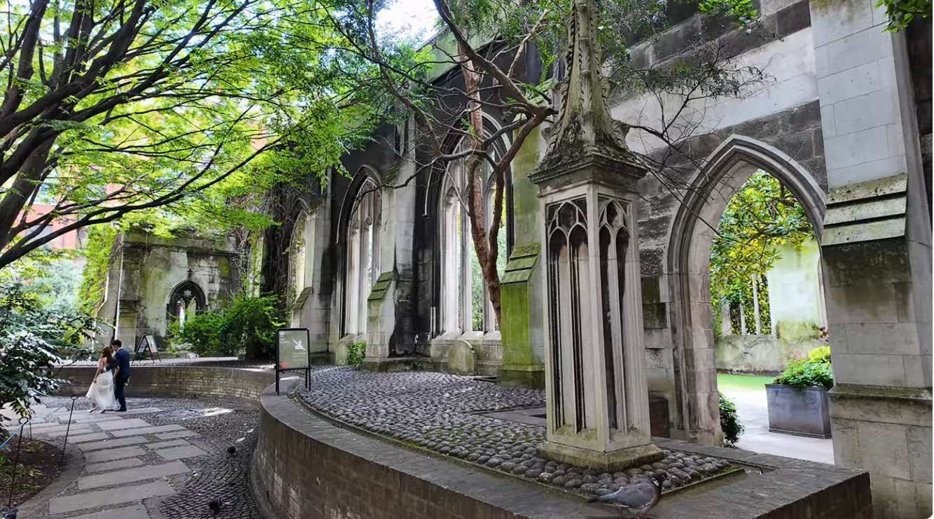 St Dunstan in the East London garden ruins with Gothic arches, stone columns, trees, and cobbled pathway in historic church setting.