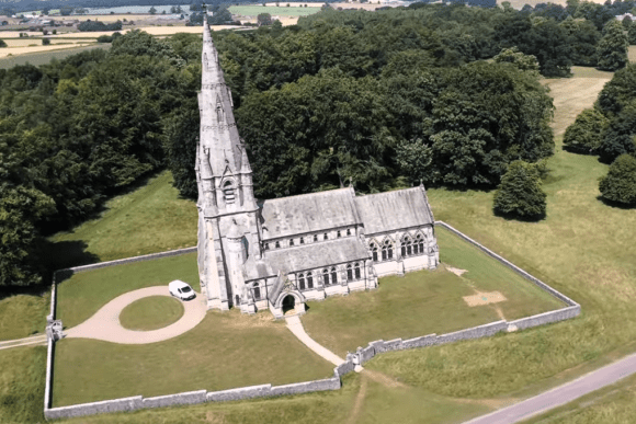 St Mary’s Church Studley Royal aerial view with tall Gothic spire, stone building, and surrounding countryside in North Yorkshire.