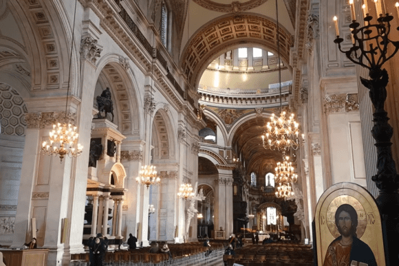 Interior of St Paul’s Cathedral London showing grand arches, chandeliers, ornate ceiling, and central nave with visitors.
