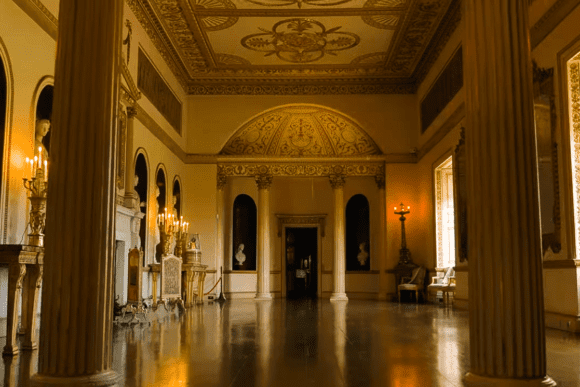 Elegant neoclassical interior hall at Syon House with grand columns, ornate ceilings, chandeliers, and polished floors.