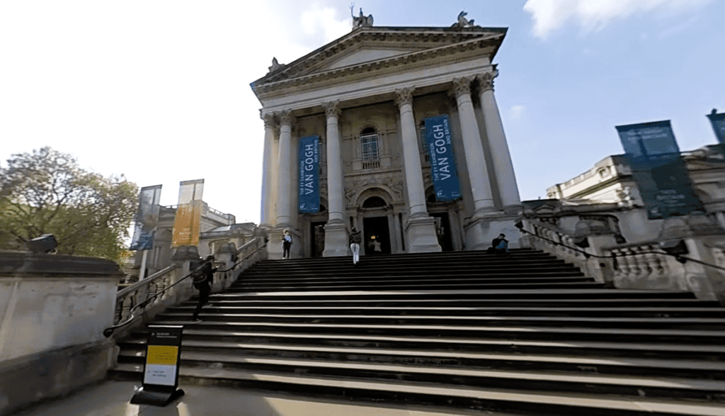 Front entrance of Tate Britain in Millbank, London, featuring grand neoclassical columns, wide stone steps, and exhibition banners.