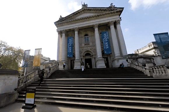Front entrance of Tate Britain in Millbank, London, featuring grand neoclassical columns, wide stone steps, and exhibition banners.