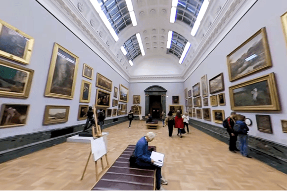 Art gallery hall inside Tate Britain in London displaying framed paintings, skylights, and visitors exploring British artworks.