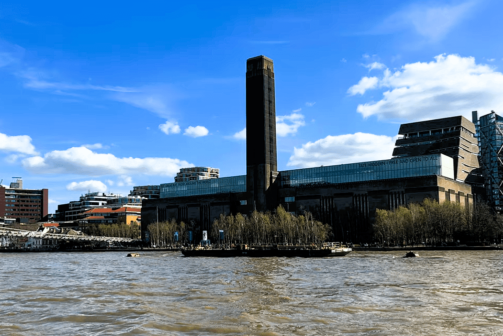 Tate Modern on London’s South Bank beside the River Thames, featuring the iconic former power station building and tall chimney.
