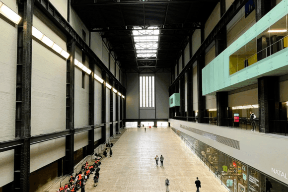 Interior of Tate Modern’s Turbine Hall in London featuring vast industrial architecture, steel beams, skylights, and visitors exploring the gallery space.