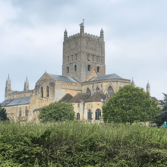 Tewkesbury Abbey in Gloucestershire viewed across landscaped gardens, featuring its historic Norman tower and medieval church architecture.