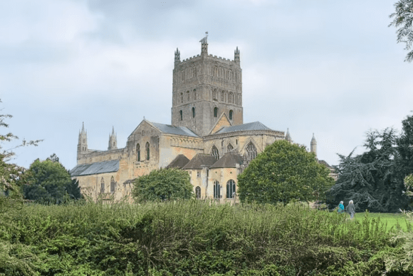 Tewkesbury Abbey in Gloucestershire viewed across landscaped gardens, featuring its historic Norman tower and medieval church architecture.