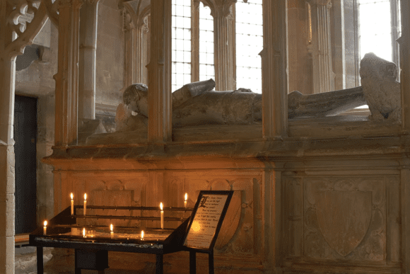 Medieval stone tomb inside Tewkesbury Abbey with lit candles, Gothic arches, and historic memorial carvings.