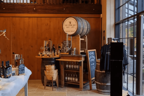 Cotswolds Distillery visitor shop featuring whisky and gin bottles, tasting station, oak cask display, and tour information in the Cotswolds, England.