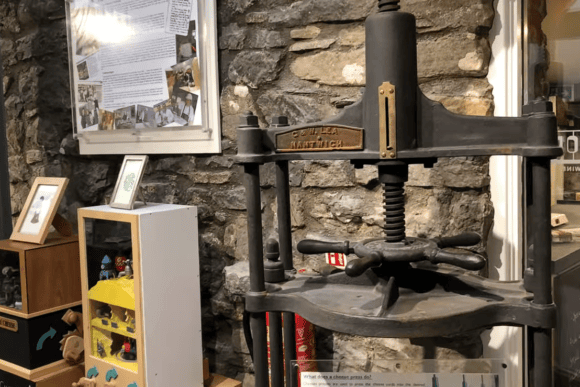 Historic cast iron cheese press displayed at The Courtyard Dairy museum alongside traditional cheese-making exhibits and educational displays.