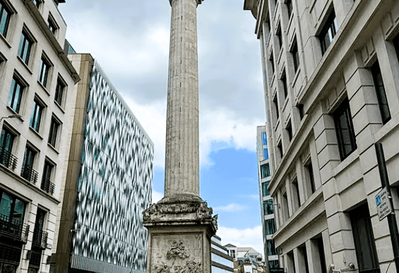 The Monument to the Great Fire of London standing tall in the City of London between modern buildings and historic streets.