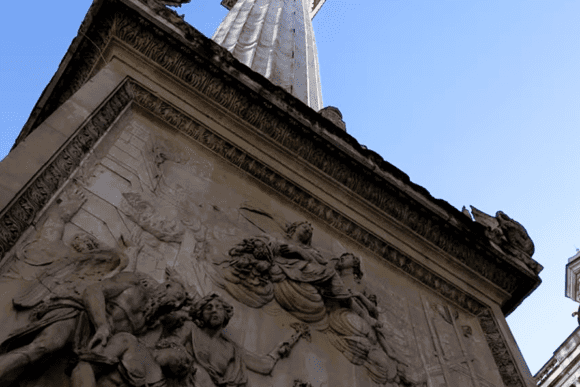 Close-up view of The Monument to the Great Fire of London featuring detailed stone carvings and the towering column against a blue sky.