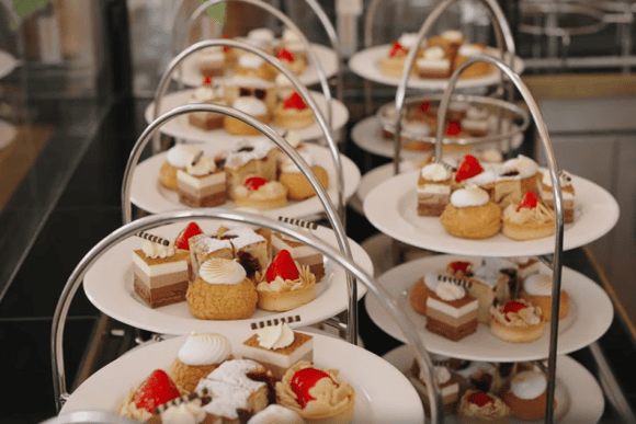 Elegant afternoon tea stands at The Pump Room Restaurant in Bath featuring an assortment of miniature cakes, pastries, fruit tarts, cream-filled desserts, and fresh strawberries.