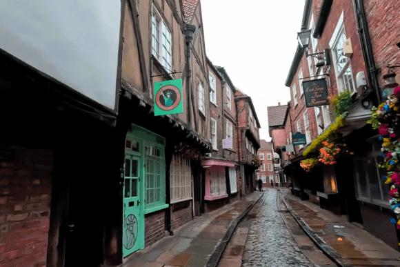 Cobbled street lined with medieval timber-framed buildings and colourful shopfronts along The Shambles in York, England.